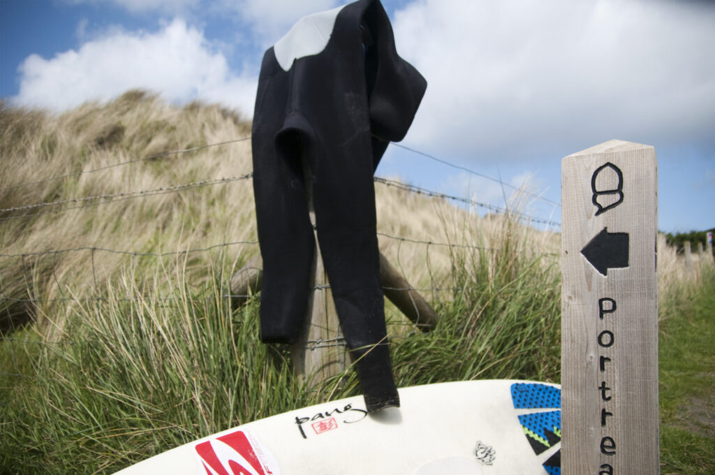 Surfboard and wetsuit, with the footpath sign for Portreath, at Godrevy, Cornwall