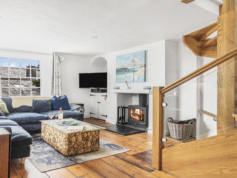 Cozy living room in Cornish Secrets cottage with fireplace and wooden staircase, seaside decor, perfect for relaxing Cornwall holidays.
