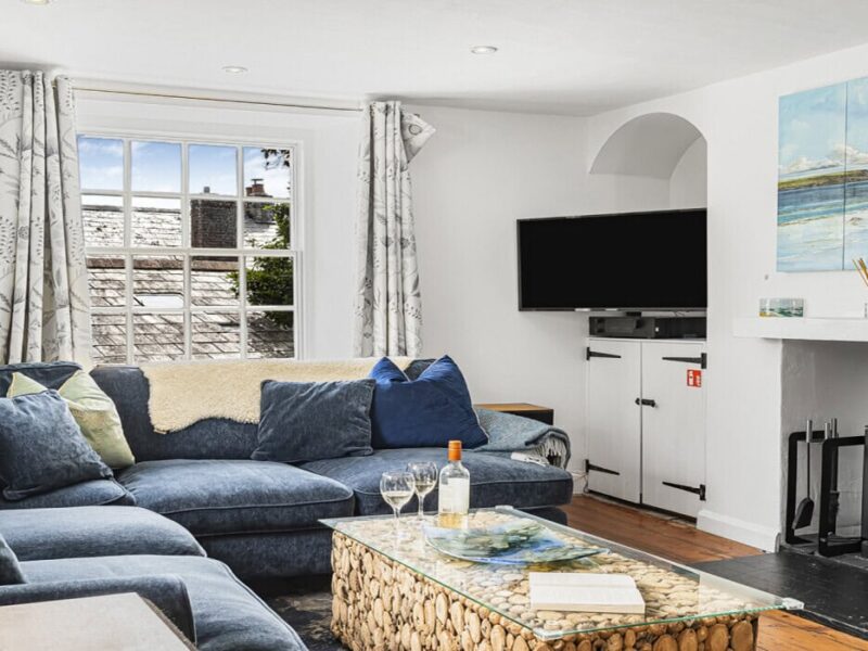 Cozy Cornish cottage living room with wood-burning stove and seaside artwork.