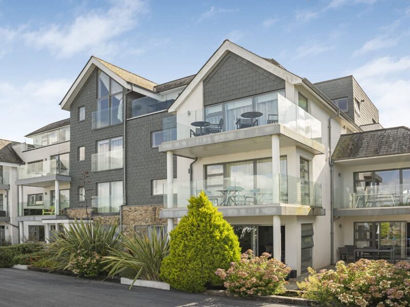 Modern seaside apartment building in Cornwall, with glass balconies and lush garden landscaping.