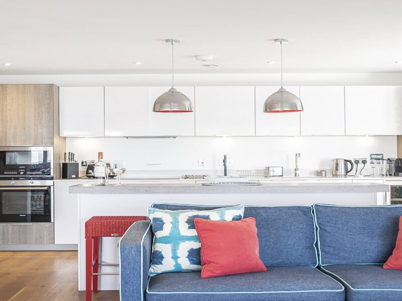 Modern open-plan kitchen and lounge area at Cornish Secrets holiday accommodation, featuring stylish decor and vibrant cushions.