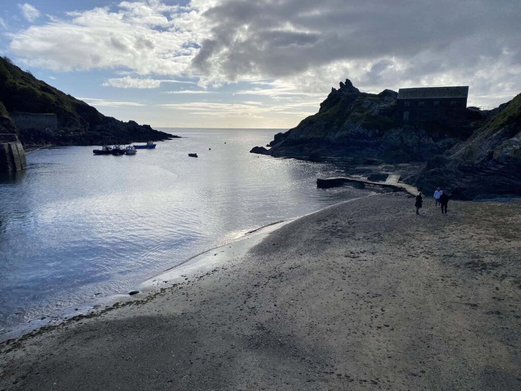 Seaside cove with boats and dramatic cliffs in Cornwall, ideal for coastal holidays.