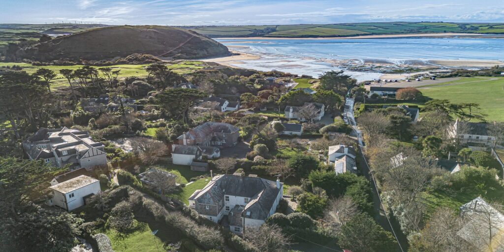 Panoramic aerial view of Cornish seaside village near the coast, featuring lush greenery, charming houses, and sandy beaches.