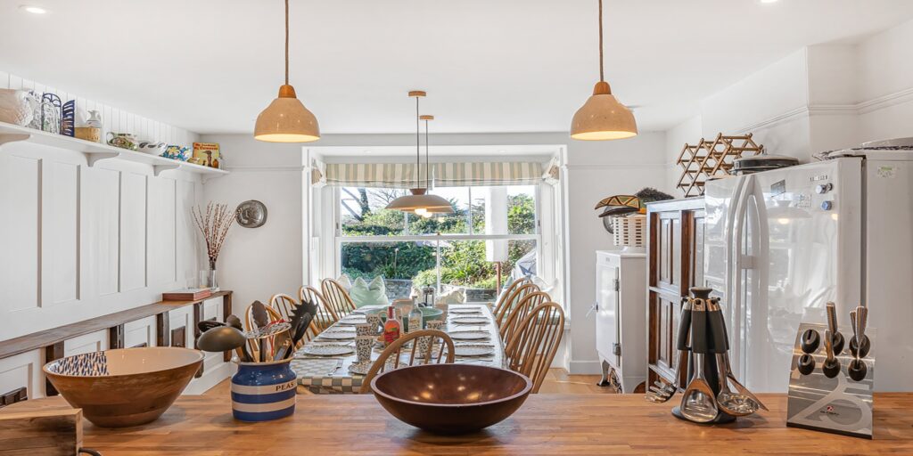 Bright, airy Cornish holiday home kitchen with country-style decor and large dining table.