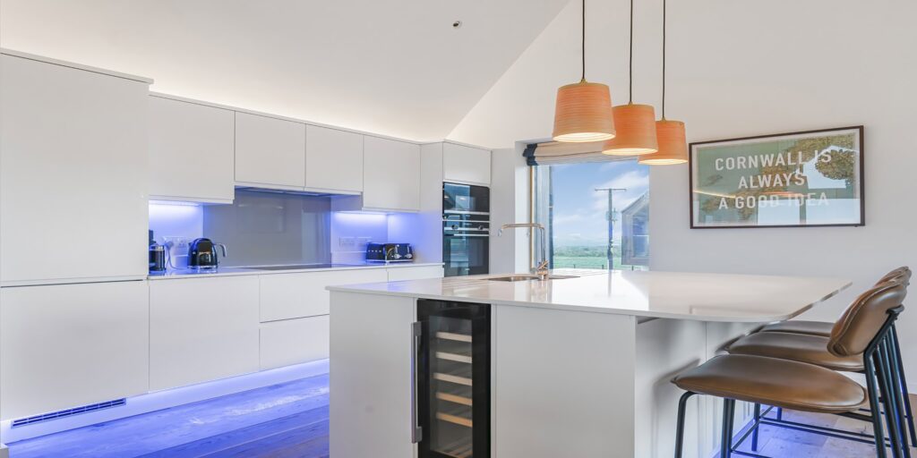 Modern white kitchen with blue LED lighting, open view, and stylish bar stools, Cornish Secrets.