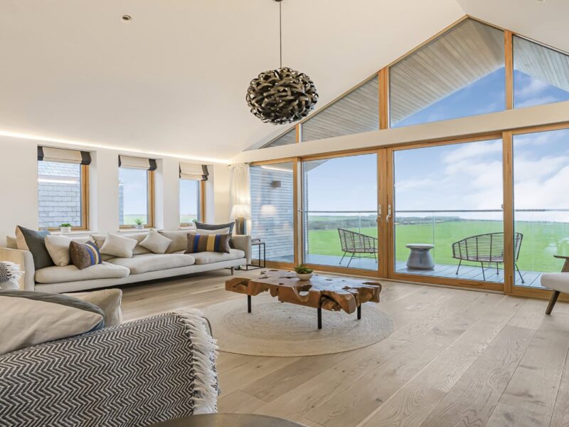 Stunning modern living room with large glass windows overlooking scenic Cornish countryside.