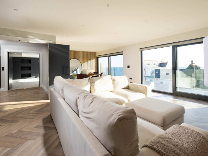 Bright living room with large windows showcasing coastal views, elegant furniture, and contemporary decor.