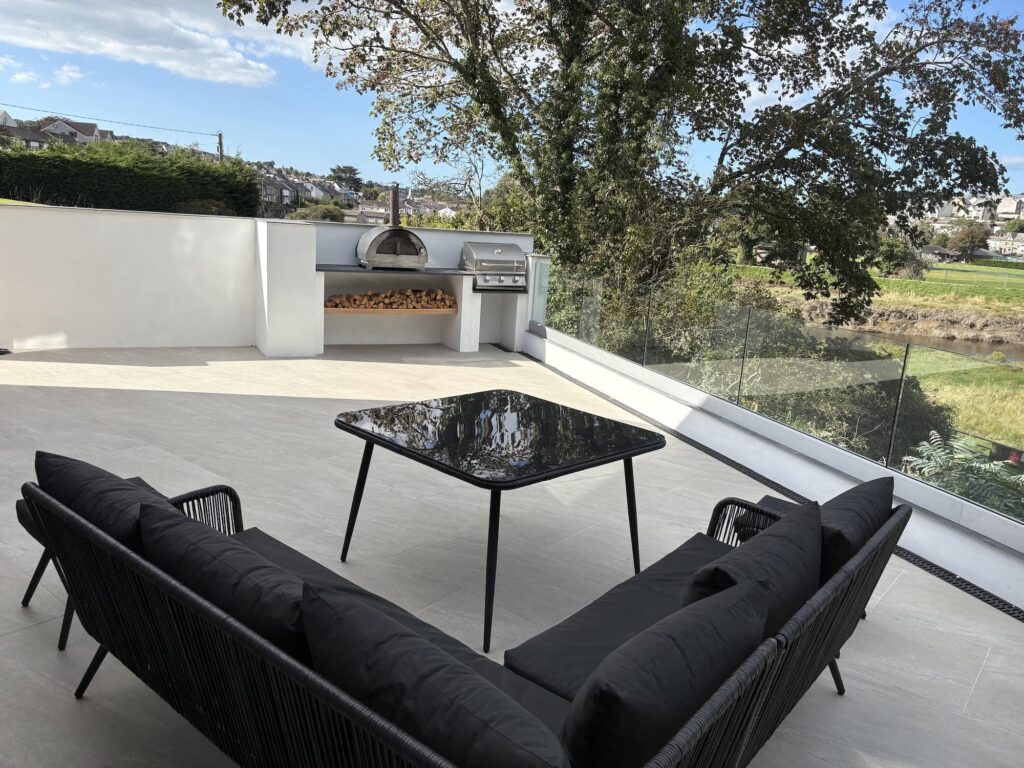 Stunning outdoor terrace featuring modern black furniture, built-in BBQ, and scenic river views in Cornwall.