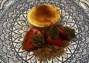 Delicious lemon tart with strawberries and edible leaves on a decorative plate.