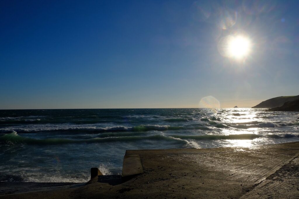 Sunset over Cornish coast with ocean waves and rocky shoreline.