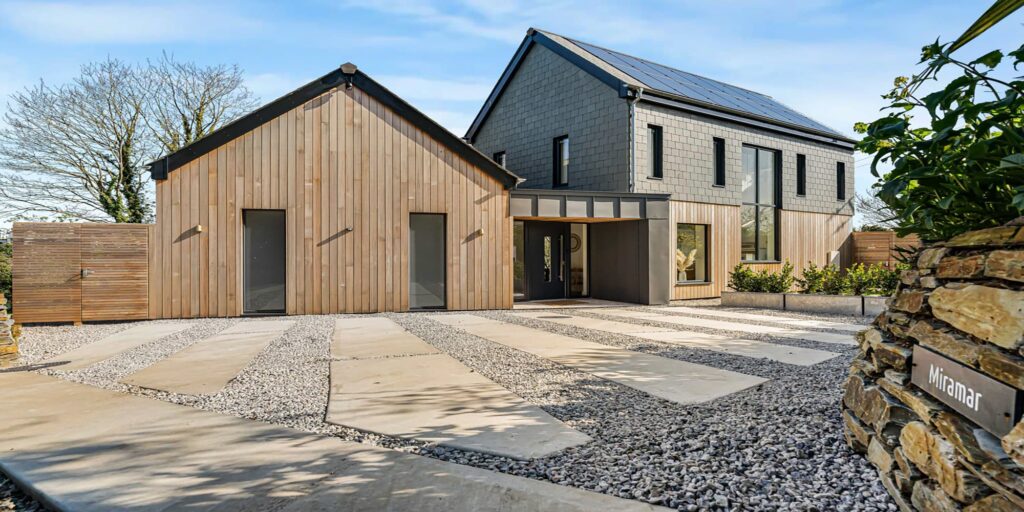 Contemporary Cornish holiday home with wooden and grey facade, surrounded by a gravel driveway and l.