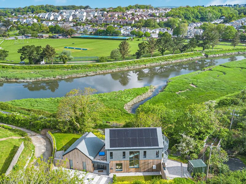 Countryside and river scene with lush greenery and a modern house in Cornwall.