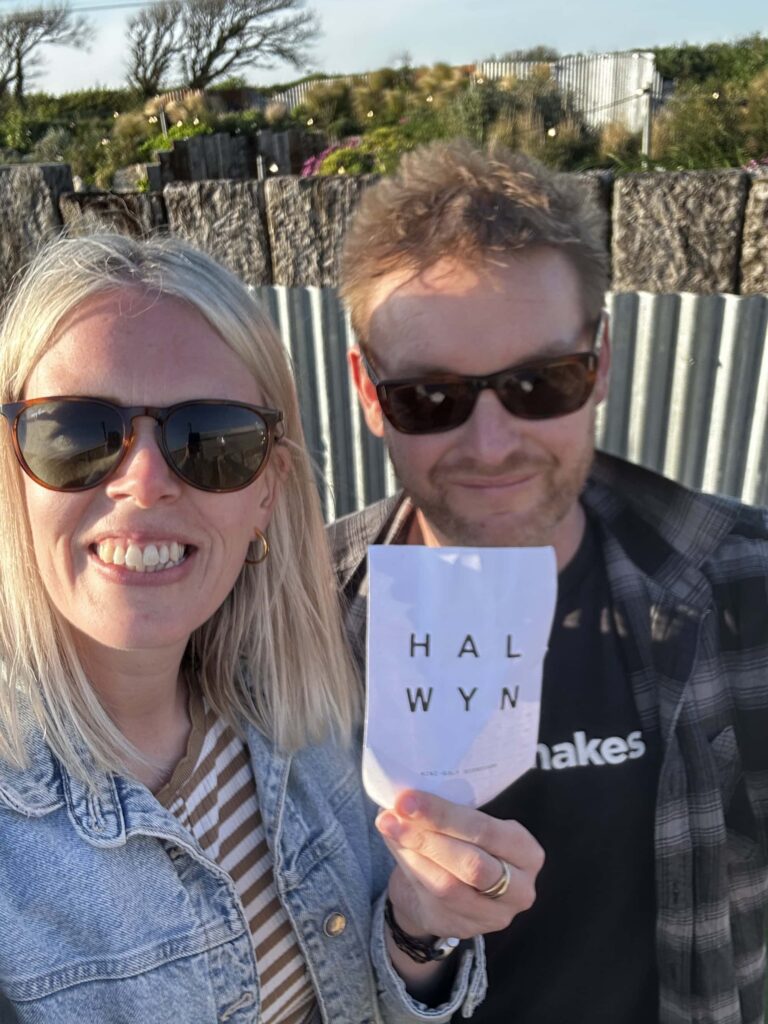 Happy couple enjoying sunny day in Cornwall, holding a Cornish Secrets sign.